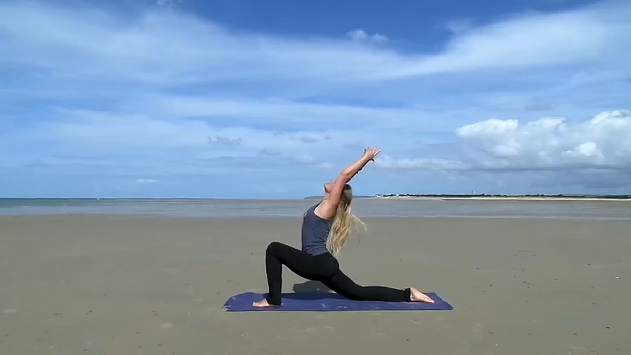 Caroline van den Ende in een lage lunge met de armen omhoog op een breed strand in Frankrijk