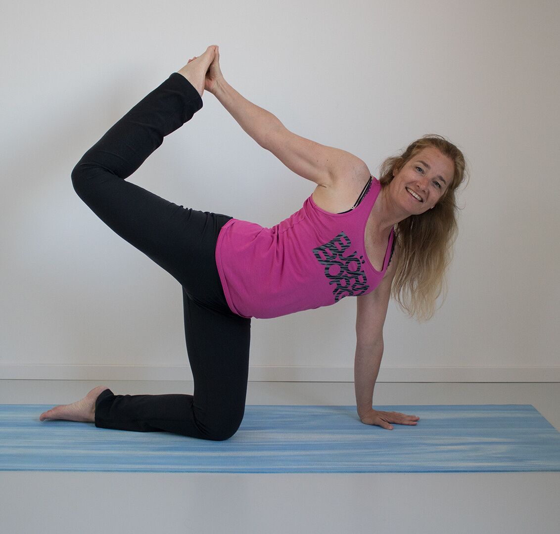 Caroline van den Ende lachend in een balanshouding op de yogamat, met één voet in haar hand