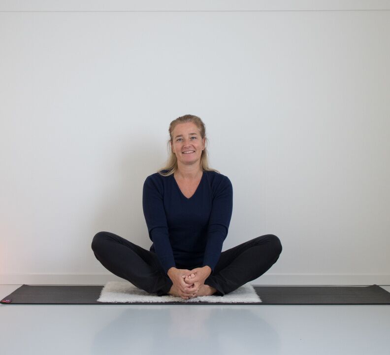 Caroline van den Ende zit lachend in kleermakerszit op de yogamat
